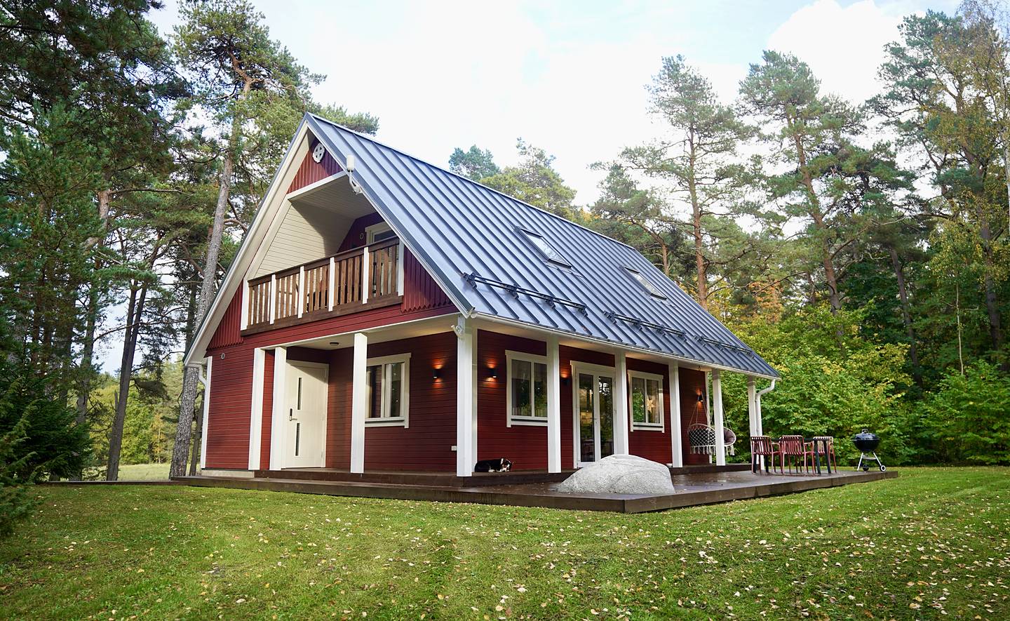 Det faluröda huvudhuset med balkong och terrass bland tallarna